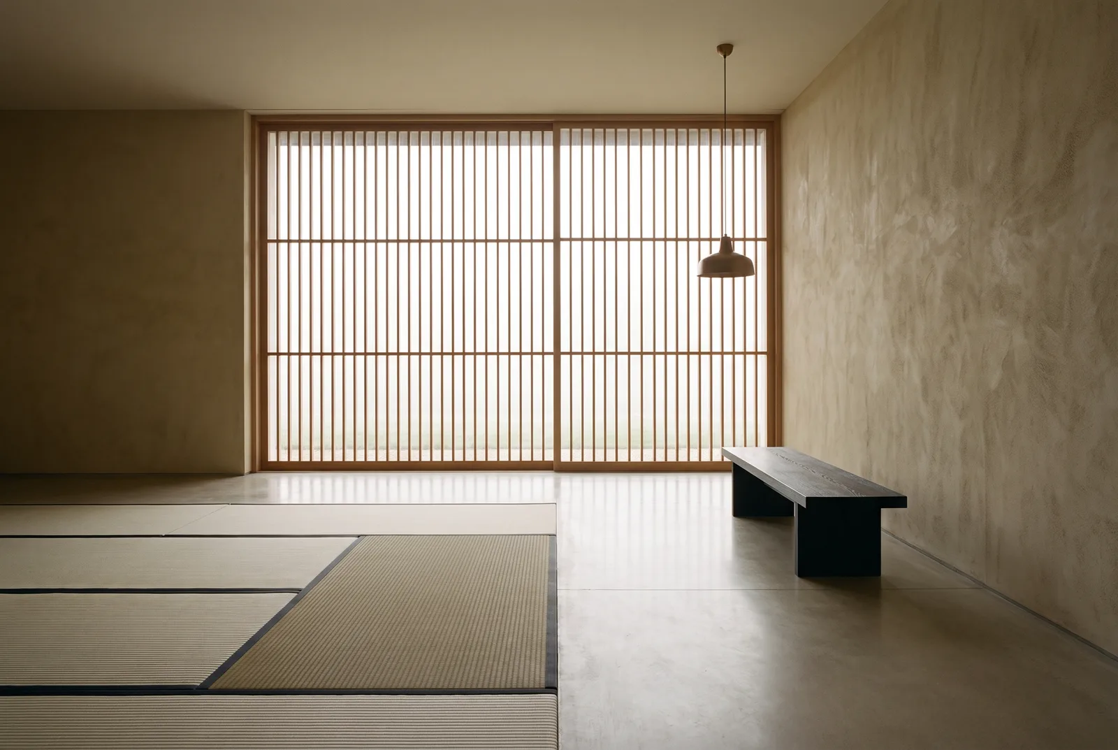 A quiet interior where tatami mats meet a polished concrete floor; fog-white light filters through a full-height timber screen beside a low dark bench.